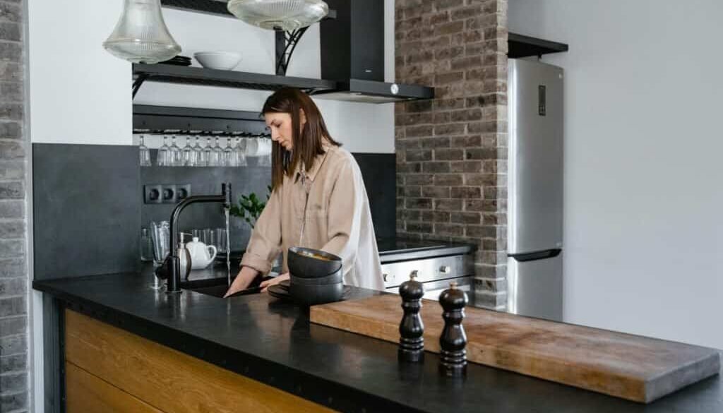 Young woman washing dishes in a contemporary kitchen setting with brick accents.