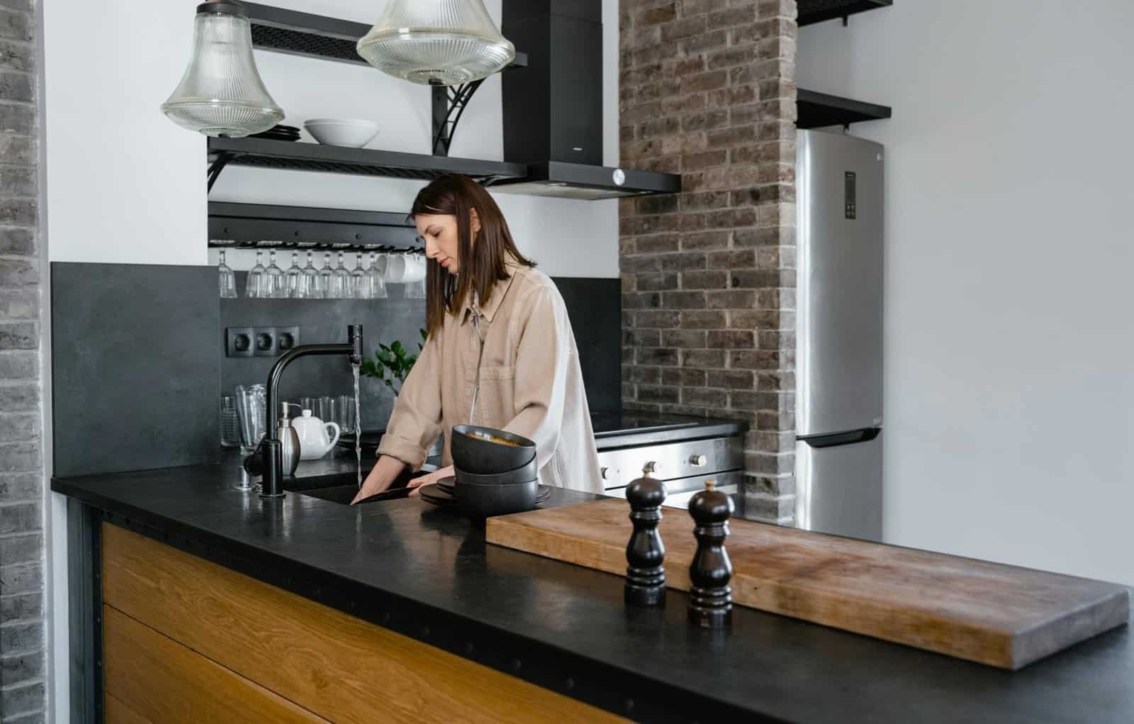 pexels-photo-7641007-7641007 Young woman washing dishes in a contemporary kitchen setting with brick accents.